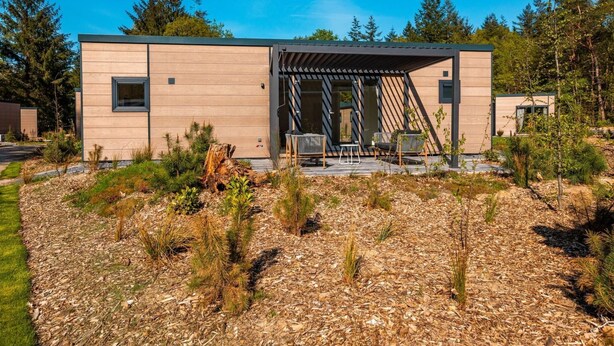 Uma cabana moderna com área de estar coberta ao ar livre, rodeada por paisagem natural.