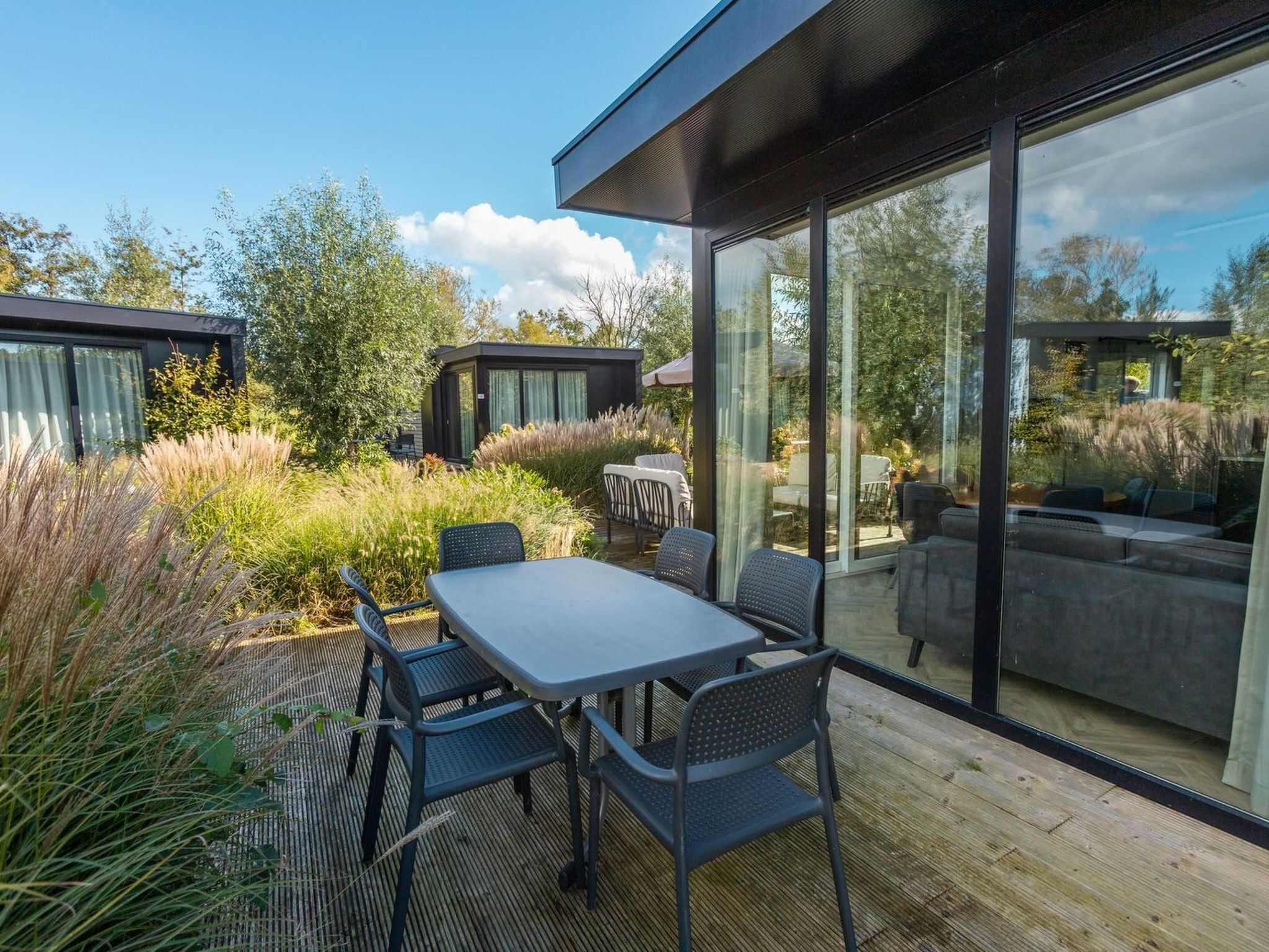 Eine moderne Terrassenanlage im Freien mit Tisch und Stühlen, umgeben von üppiger Bepflanzung und großen Fenstern.
