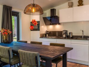 Een moderne keuken met een eethoek, met een donker houten tafel, groene bekleden stoelen en een hangende lamp.