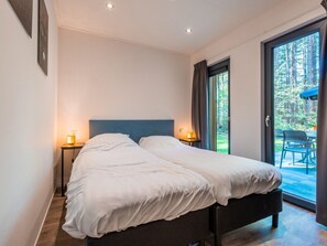 Een tweepersoonsbed met een donker hoofdbord in een kamer met een grote schuifdeur naar een buitenruimte.