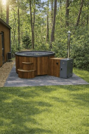 Een hottub in een bebost gebied met een houten terras en een metalen heater.