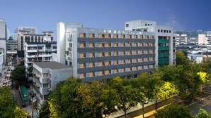 Un hotel de varios pisos con una fachada moderna, situado en un entorno urbano rodeado de edificios.