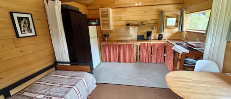 Una cabaña compacta con kitchenette, comedor y cama con colcha estampada.