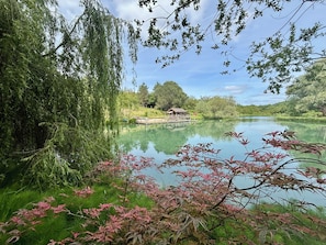 A serene lakeside scene with a wooden dock and a small building, surrounded by lush greenery and trees.