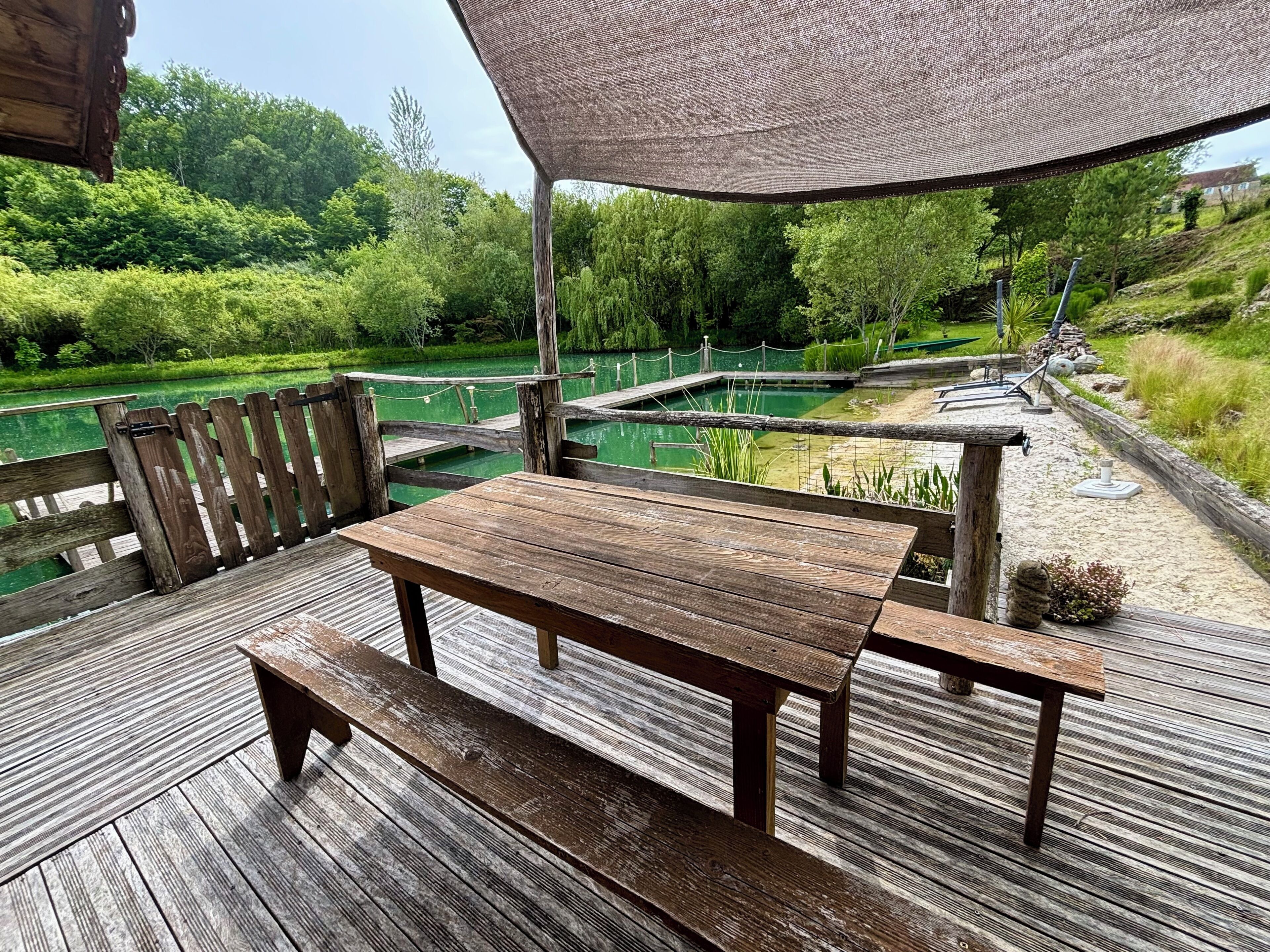 A wooden deck with a table and benches overlooking a pond with a wooden bridge.