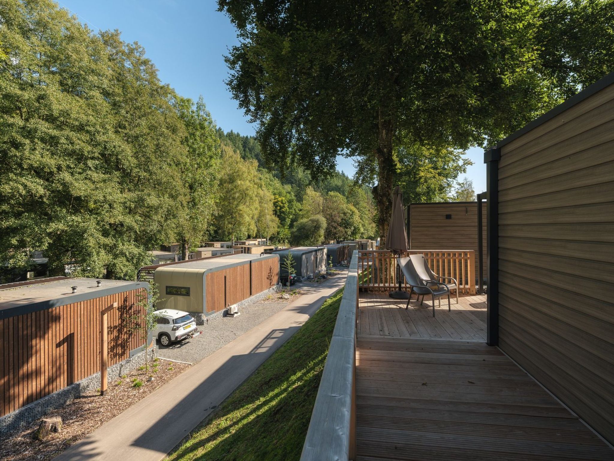 A campsite with RVs parked along a paved road, a wooden deck, and a fenced area with a chair.
