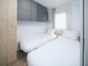 Un dormitorio moderno con dos camas individuales, un armario de madera y un mueble gris.