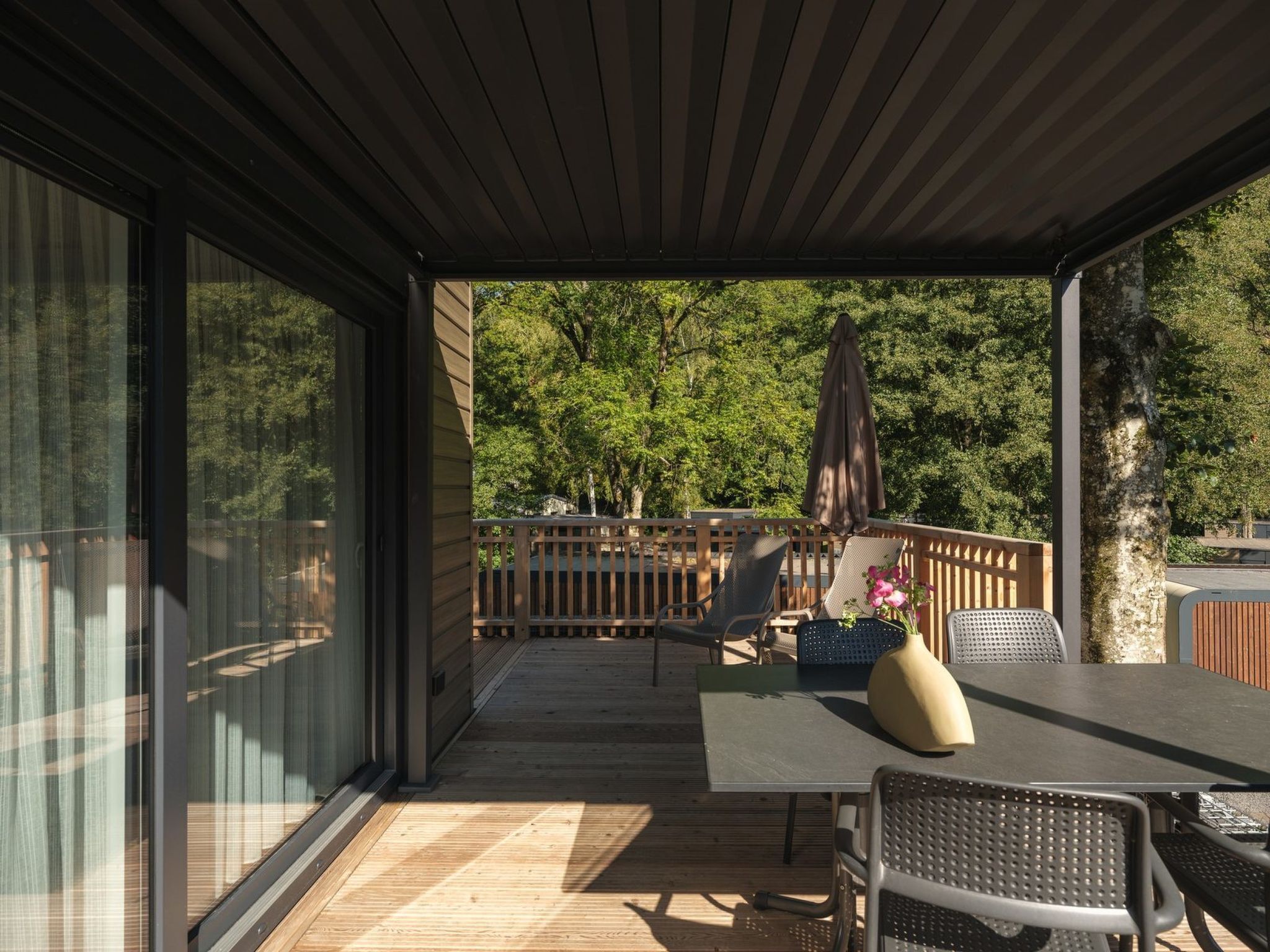Una terrazza coperta all'aperto con tavolo e sedie, un recinto in legno e vista sugli alberi.