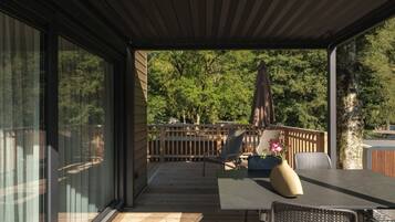 Una terrazza coperta all'aperto con tavolo e sedie, un recinto in legno e vista sugli alberi.