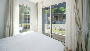 Una camera da letto con un letto grande, porte a vetri scorrevoli che danno su un balcone e vista su un edificio e del verde all'esterno.