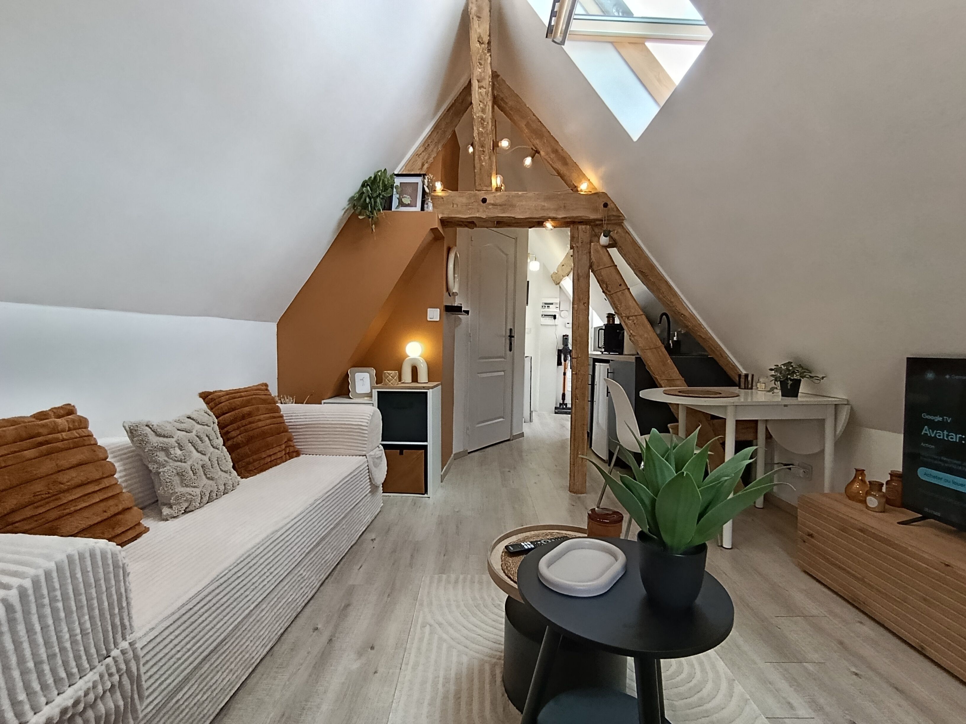 Un espace de vie de style loft avec un plafond en pente, un canapé, une petite table et un téléviseur.