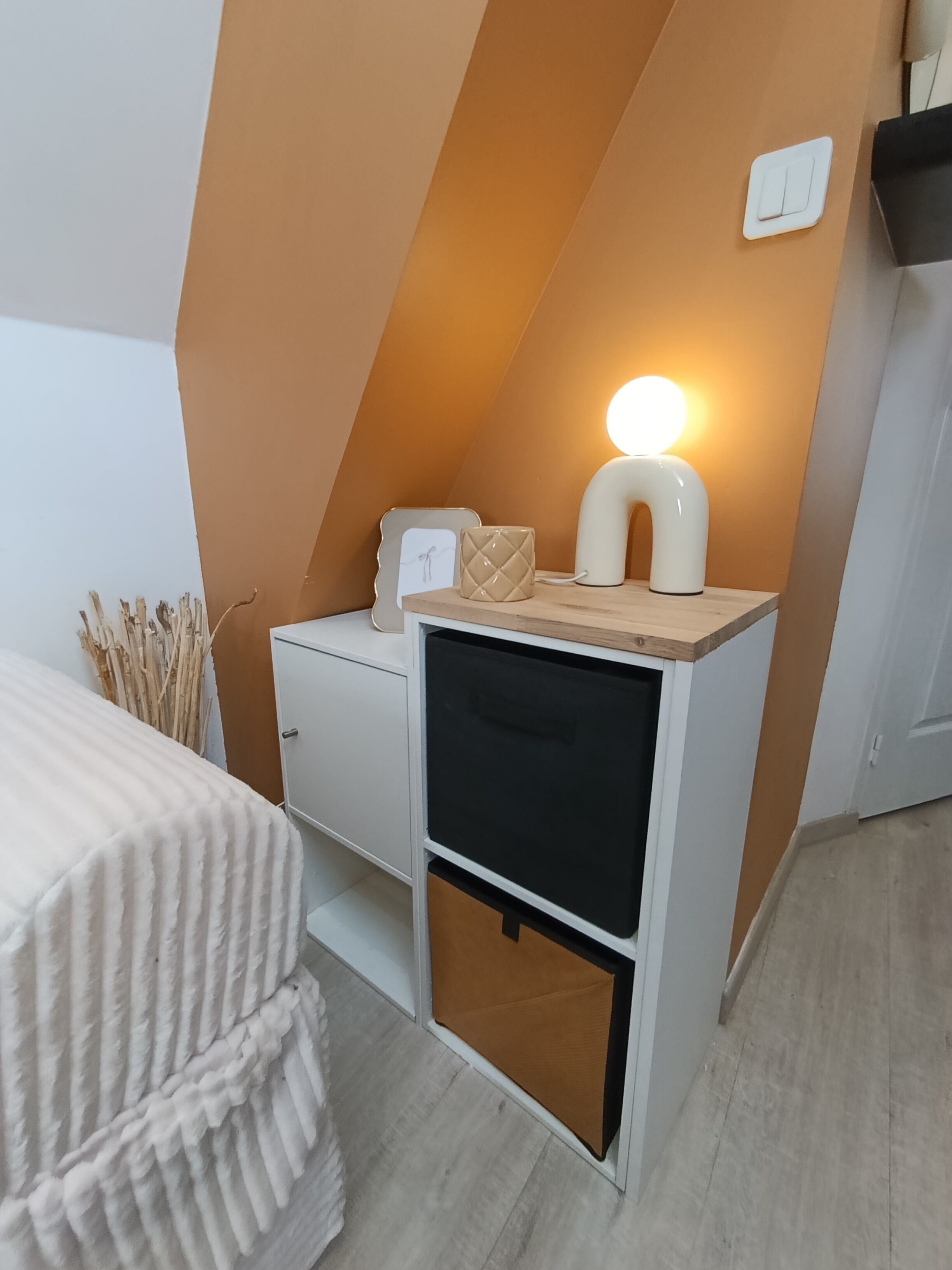 Une chambre à coucher avec un lit, une table de chevet avec une lampe, une commode et un interrupteur fixé au mur.