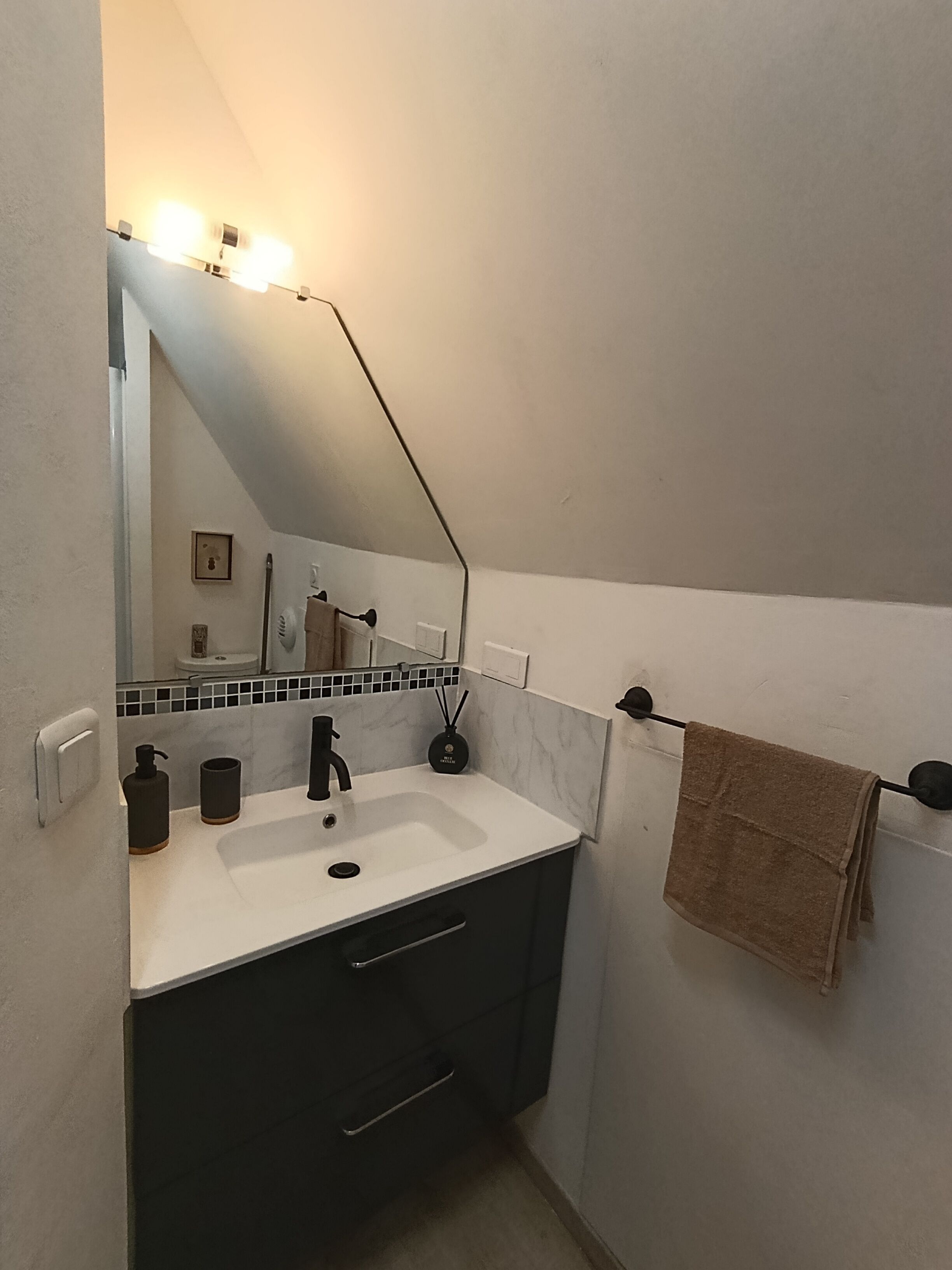 Une salle de bain avec un lavabo blanc, un meuble sombre et une serviette suspendue à un porte-serviettes.