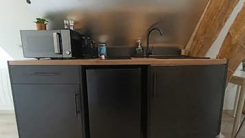 A compact kitchenette with a microwave, coffee maker, and a sink.