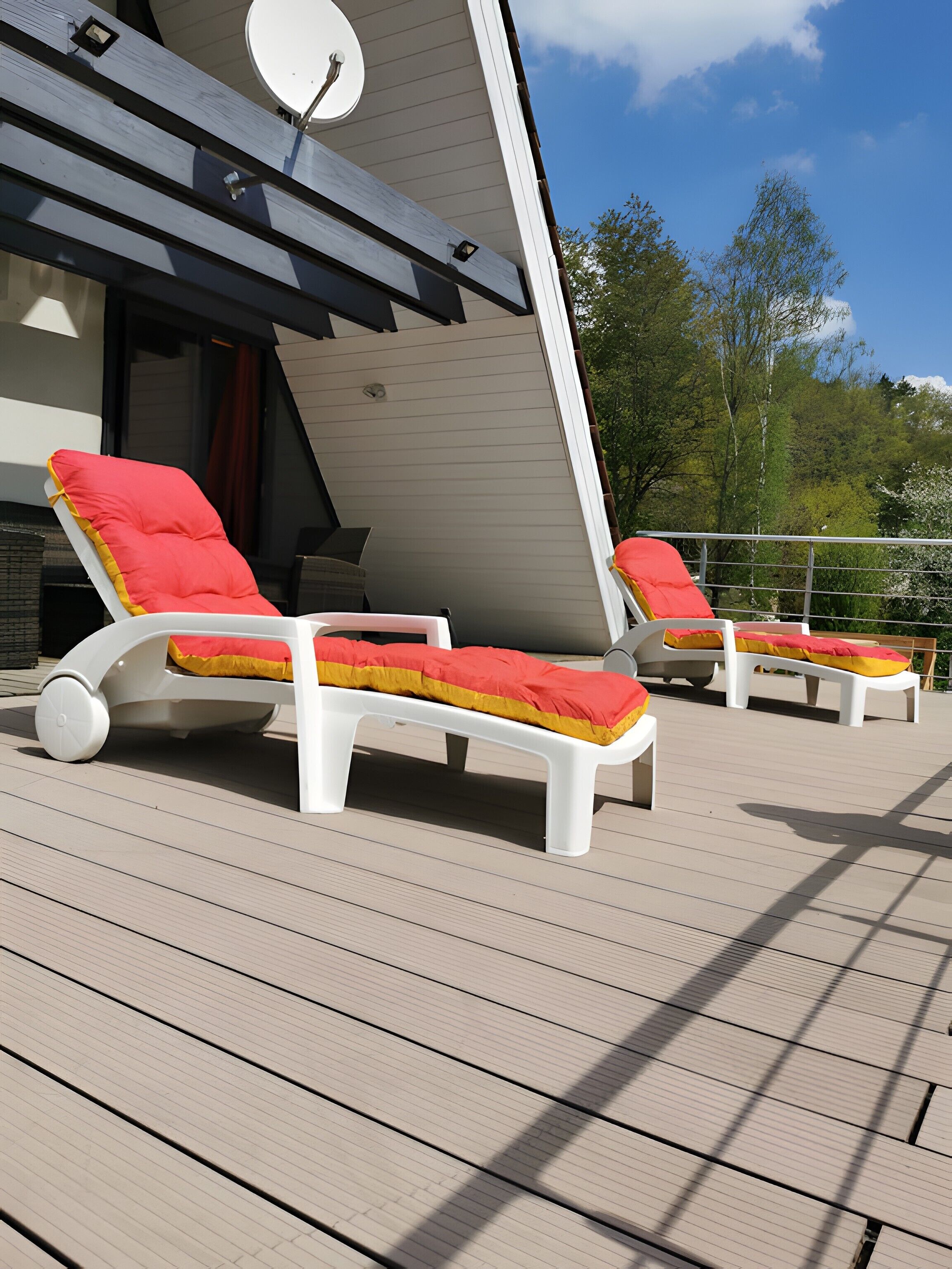A deck with two white lounge chairs, each with a red cushion.
