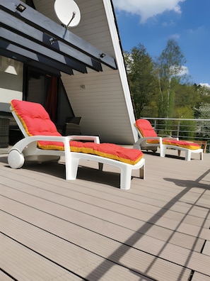 A deck with two white lounge chairs, each with a red cushion.