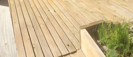 A wooden deck with a door and windows, a small trash bin, and a grassy area.