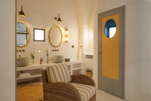 A bathroom with a round mirror, a white sink, and a wicker chair.