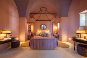 A bedroom with a four-poster bed, bedside tables, a round mirror, and a view of a room with a pink wall and a window. - Palazzo Ceraselli (Martina Franca)
