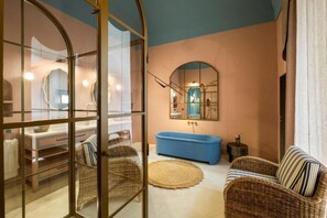 A bathroom with a blue bathtub, wicker chairs, and a round rug.