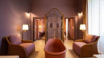 Une pièce avec deux fauteuils en osier, une baignoire centrale et un mur recouvert de miroirs.