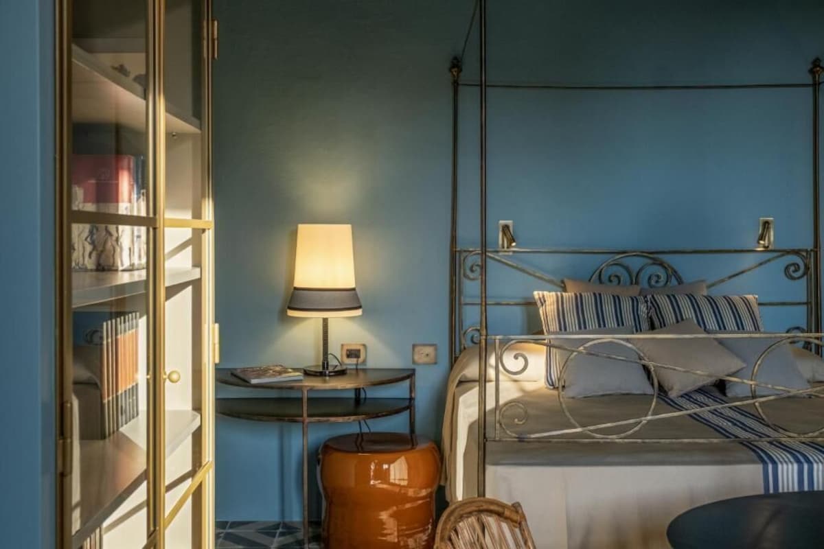 A bedroom with a bed, bedside table, lamp, and a bookshelf.