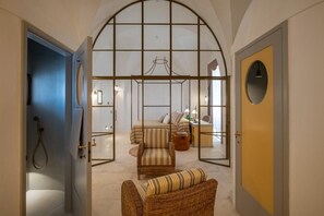 A room with a bed, a chair, a desk, and a large arched window.