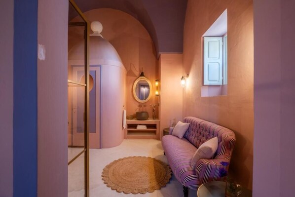 A narrow hallway with a round rug, a sofa with patterned cushions, and a wall-mounted mirror.