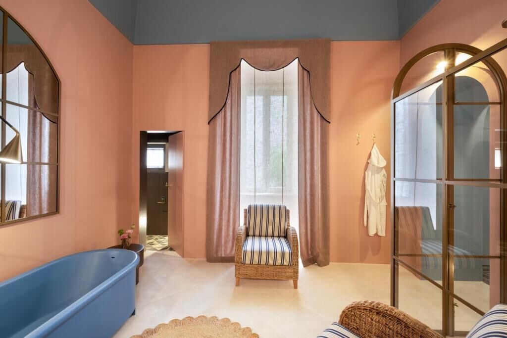 Una stanza con una vasca da bagno ampia, una poltrona in vimini e una porta in vetro.