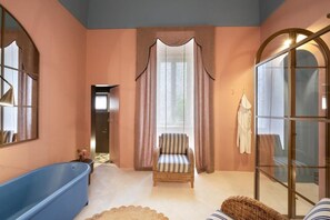 A room with a large bathtub, a wicker chair, and a glass door.