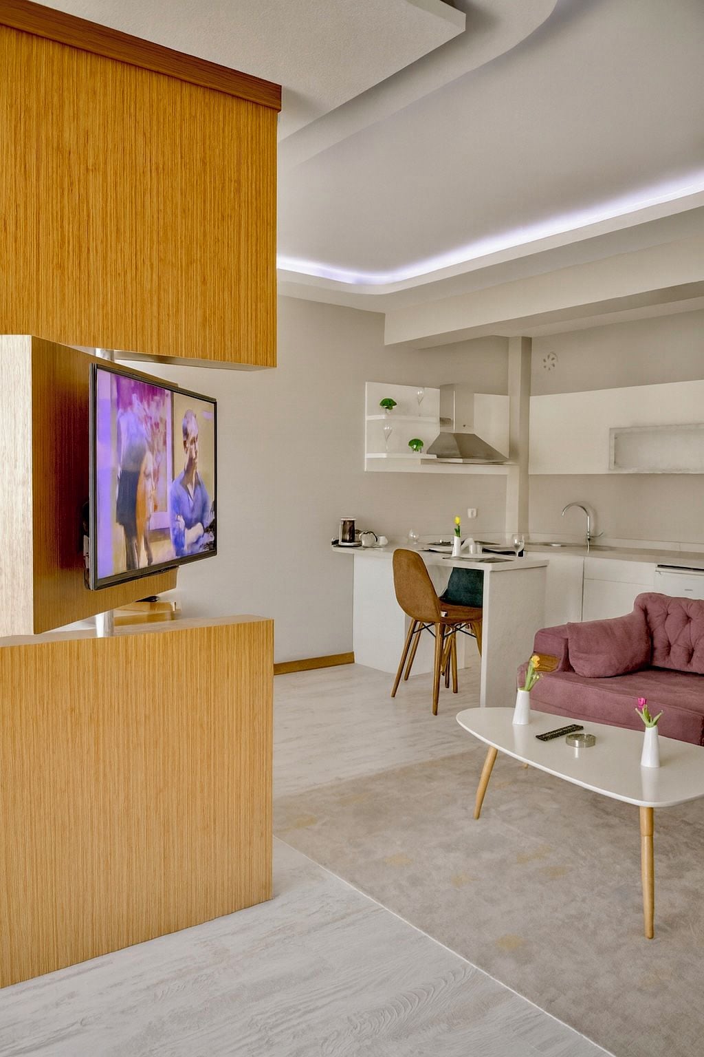 Una sala de estar moderna con un televisor de pantalla plana, un sofá rosa y una mesa de centro blanca.