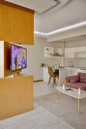 A modern living room with a flat-screen TV, a pink sofa, and a white coffee table. - THE CITY WALLS SUIT OTEL (Diyarbakir)