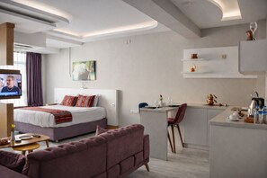 A modern hotel room with a bed, a sofa, a desk, and a kitchenette.