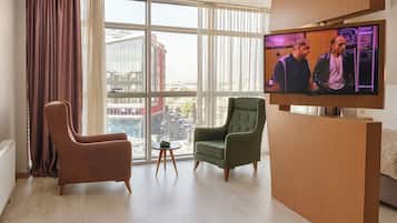 A modern hotel room with a large window, two armchairs, a small table, and a flat-screen TV.