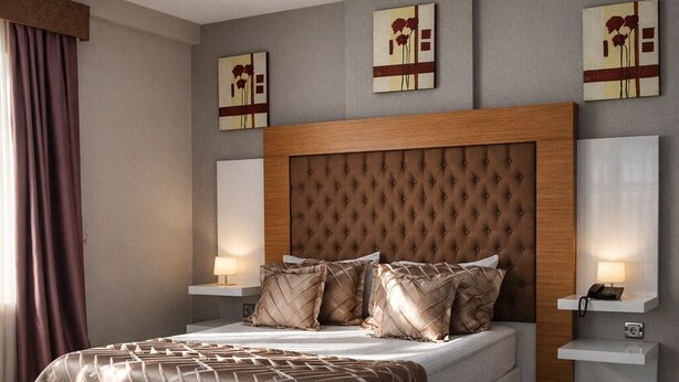 A modern bedroom with a large bed, a wooden headboard, bedside lamps, and artwork on the walls.