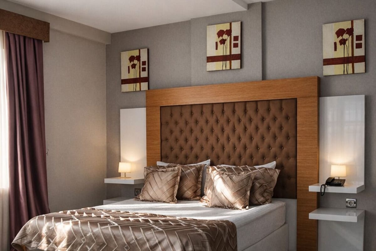 Un dormitorio moderno con una cama grande, cabecera de madera, lámparas de noche y obras de arte en las paredes.