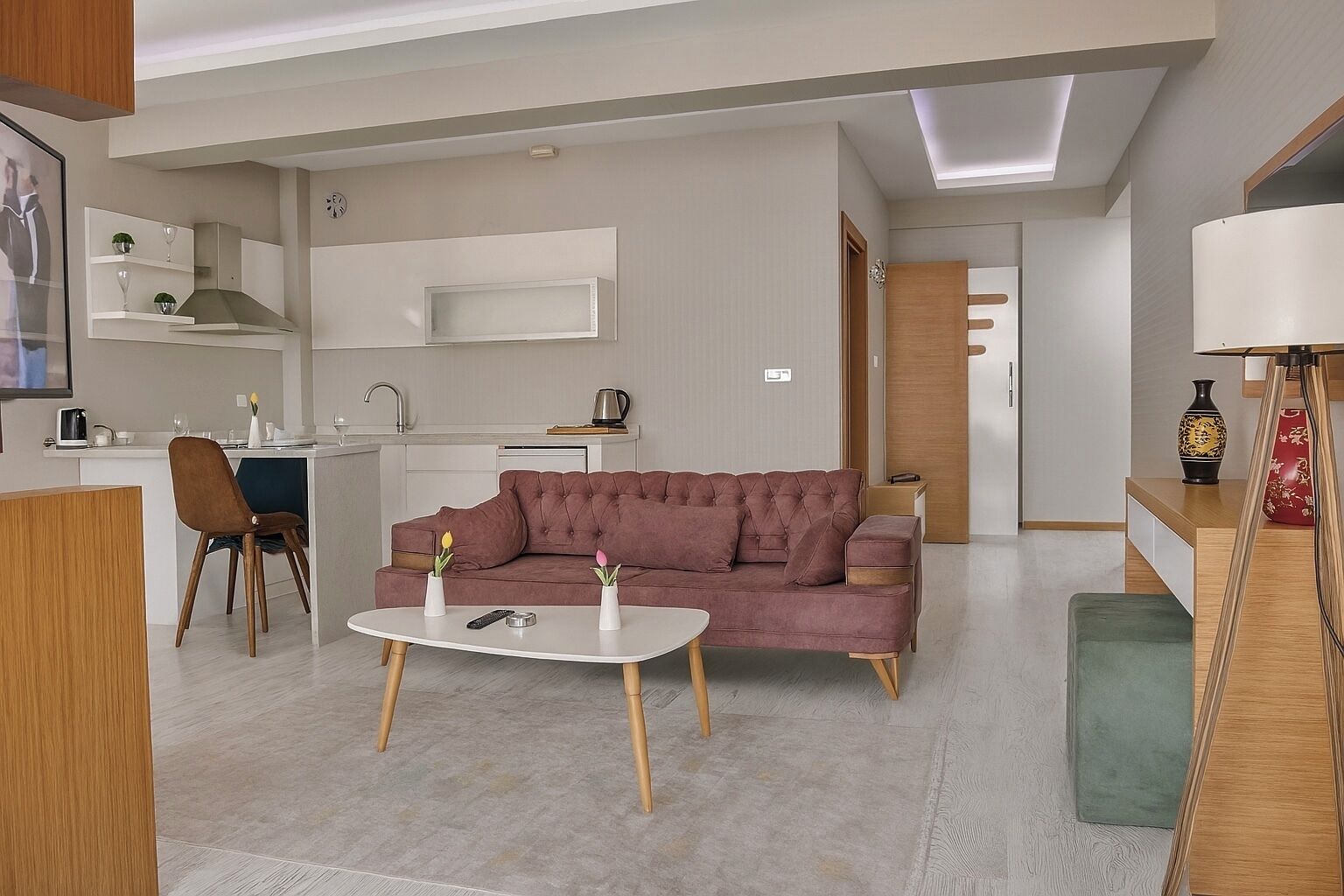 A modern living room with a sofa, coffee table, and chairs. There is a kitchen area with a sink and cabinets in the background.