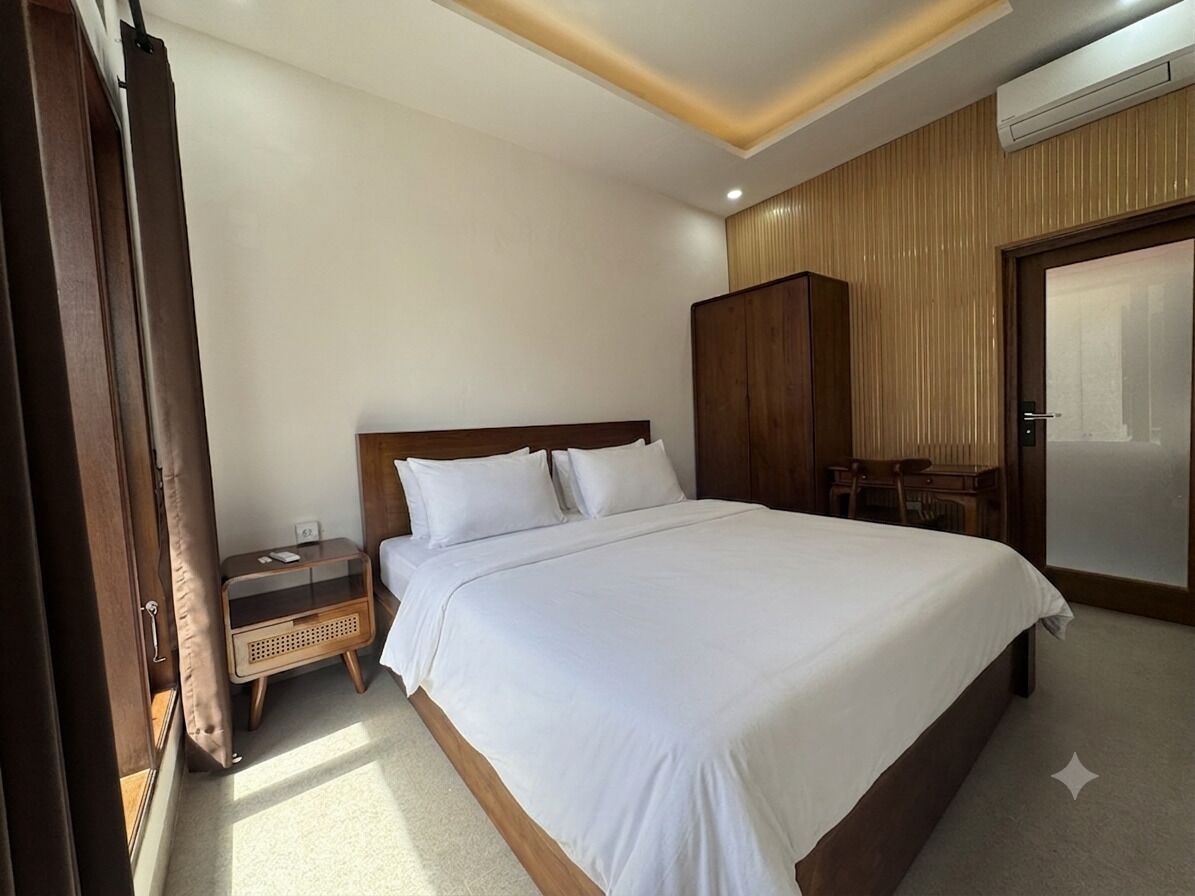 A hotel room with a large bed, a wooden wardrobe, a nightstand, and a door with a handle.