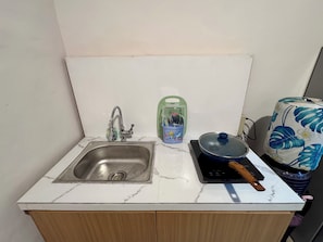 A small kitchen with a sink, a green dish soap dispenser, a blue pot on an induction cooktop, and a patterned towel.