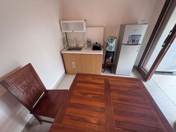 A compact kitchen with a wooden table and chair, a refrigerator, and a sink.