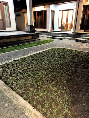 A courtyard with a paved walkway, a small garden area, and a building with a tiled roof.
