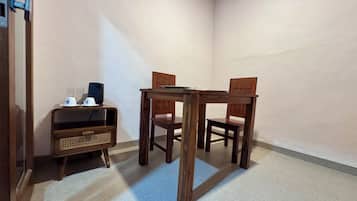 A corner room with a wooden table and chairs, a small cabinet with a radio, and a plain wall.