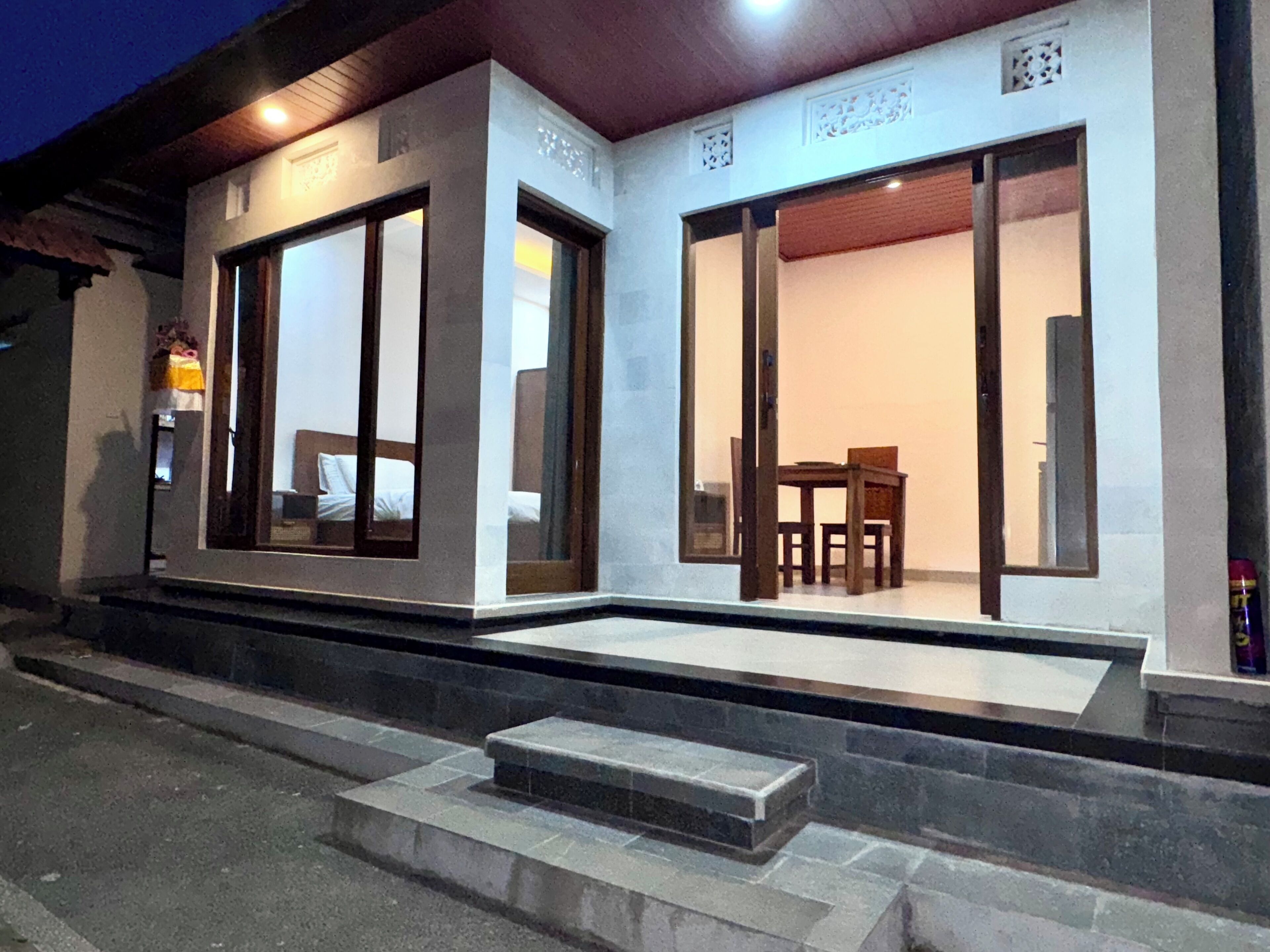A building with large sliding glass doors, a staircase leading to the entrance, and a small outdoor seating area with a table and chairs.