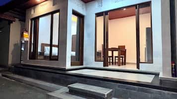 A building with large sliding glass doors, a staircase leading to the entrance, and a small outdoor seating area with a table and chairs.