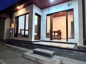 A building with large sliding glass doors, a staircase leading to the entrance, and a small outdoor seating area with a table and chairs. - Galang Homestay Ubud - Peaceful Balinese Retreat (Gianyar)