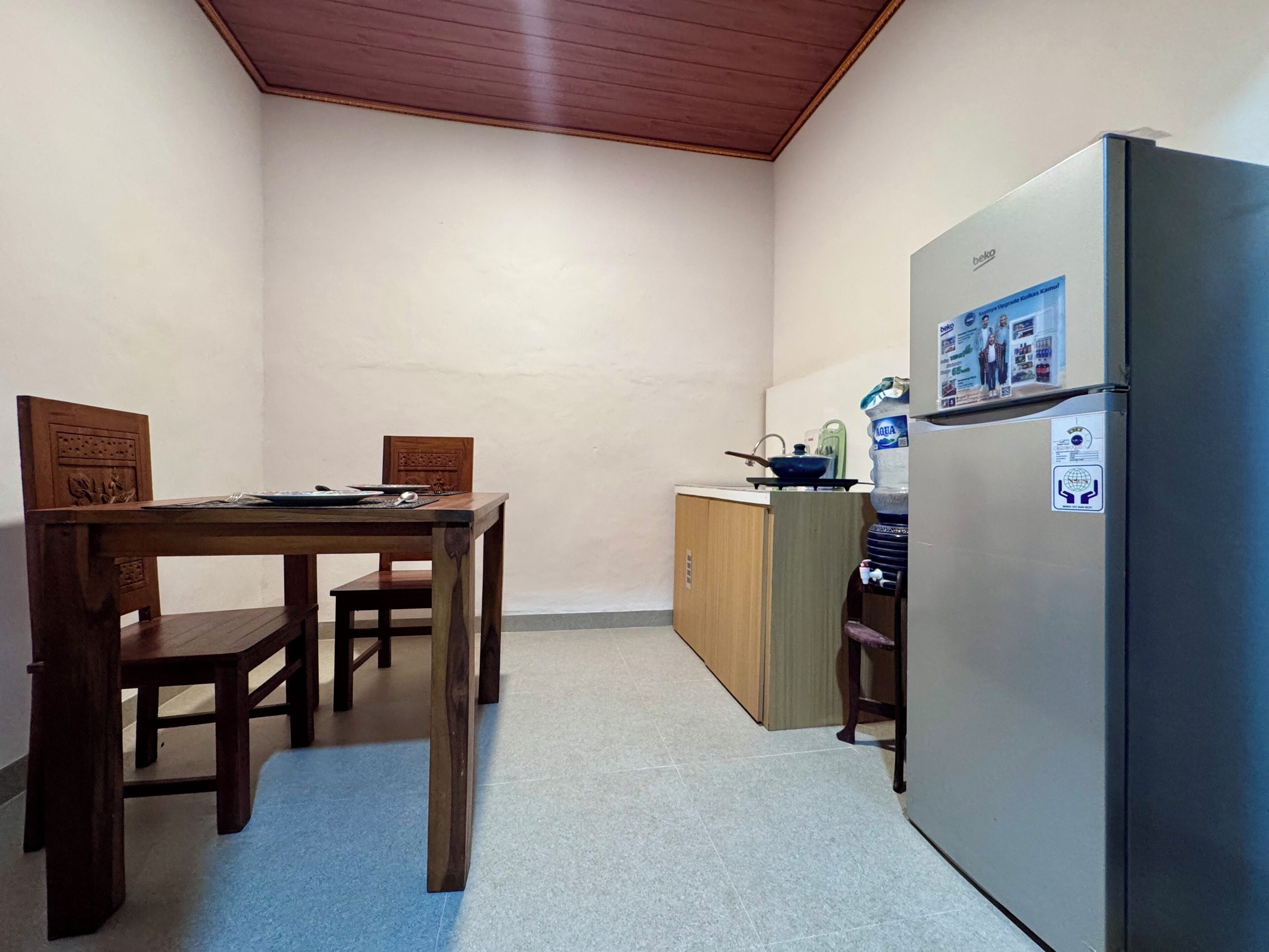 A compact kitchen with a refrigerator, wooden table, chairs, and a small countertop with a kettle.