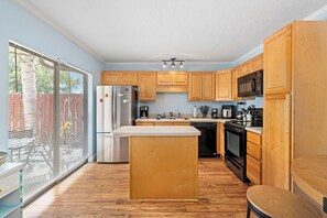 A modern kitchen with wooden cabinets, stainless steel appliances, and a large island. - Spacious two-story 2BR, 3-bath beachside condo with a private patio and upstairs balcony. Just a short drive, bike or golf cart ride to the beach. (New Smyrna Beach)