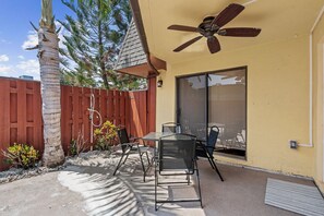 A patio with a table and chairs, a ceiling fan, a wooden fence, and a palm tree. - Spacious two-story 2BR, 3-bath beachside condo with a private patio and upstairs balcony. Just a short drive, bike or golf cart ride to the beach. (New Smyrna Beach)