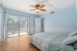 Quarto com cama, ventilador de teto e vista através de uma porta de correr de vidro.