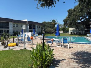 A pool area with lounge chairs and umbrellas, a swimming pool, and a building with signage. - Spacious two-story 2BR, 3-bath beachside condo with a private patio and upstairs balcony. Just a short drive, bike or golf cart ride to the beach. (New Smyrna Beach)
